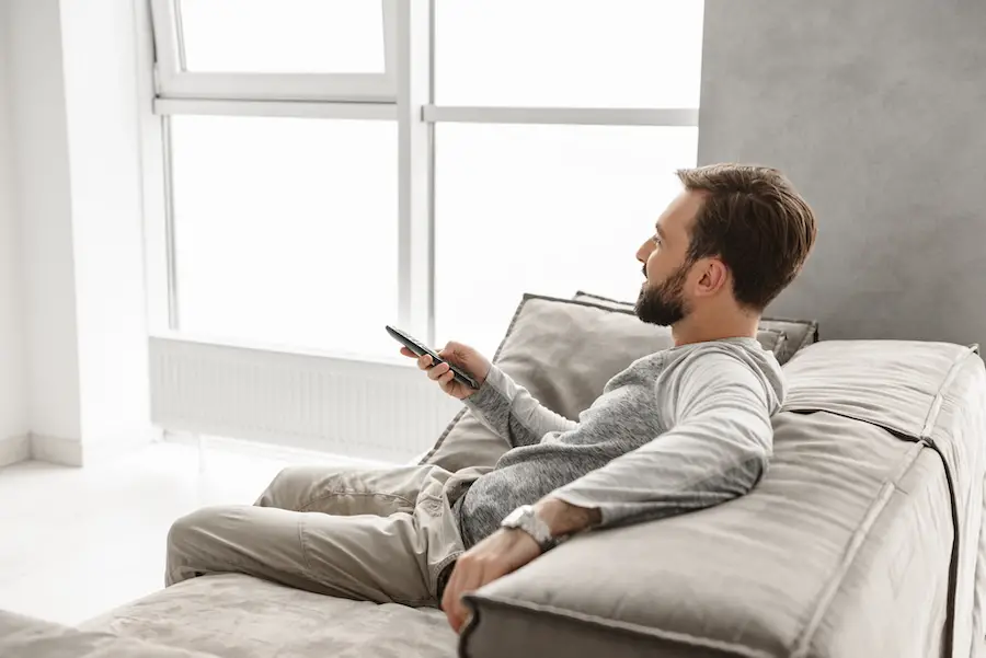 man sat on sofa holding tv remote