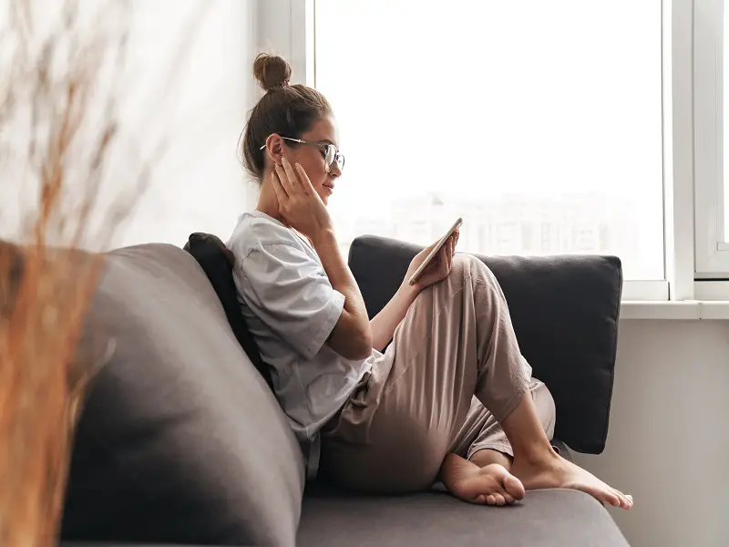 woman with glasses sat on sofa reading her mobile phone