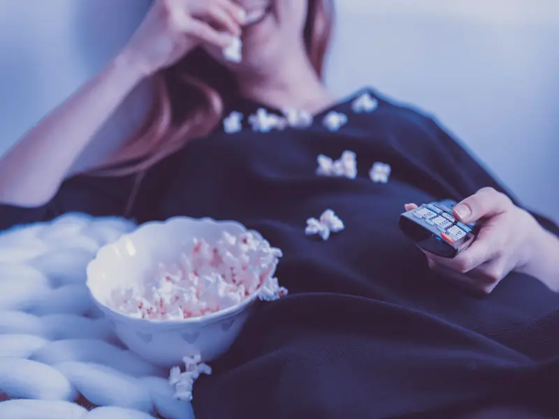 woman eating popcorn and holding tv remote