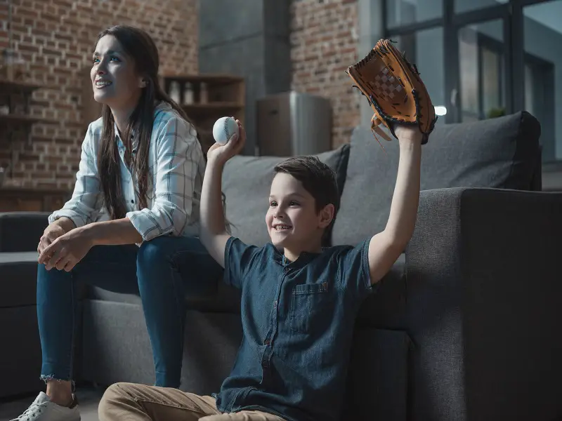 little boy cheering holding a baseball and baseball glove up 